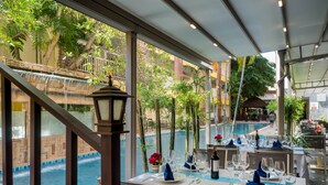 A dining area with tables set for two, overlooking a pool and lush greenery. - Tuana Hotels Casa Del Sol (Karon)