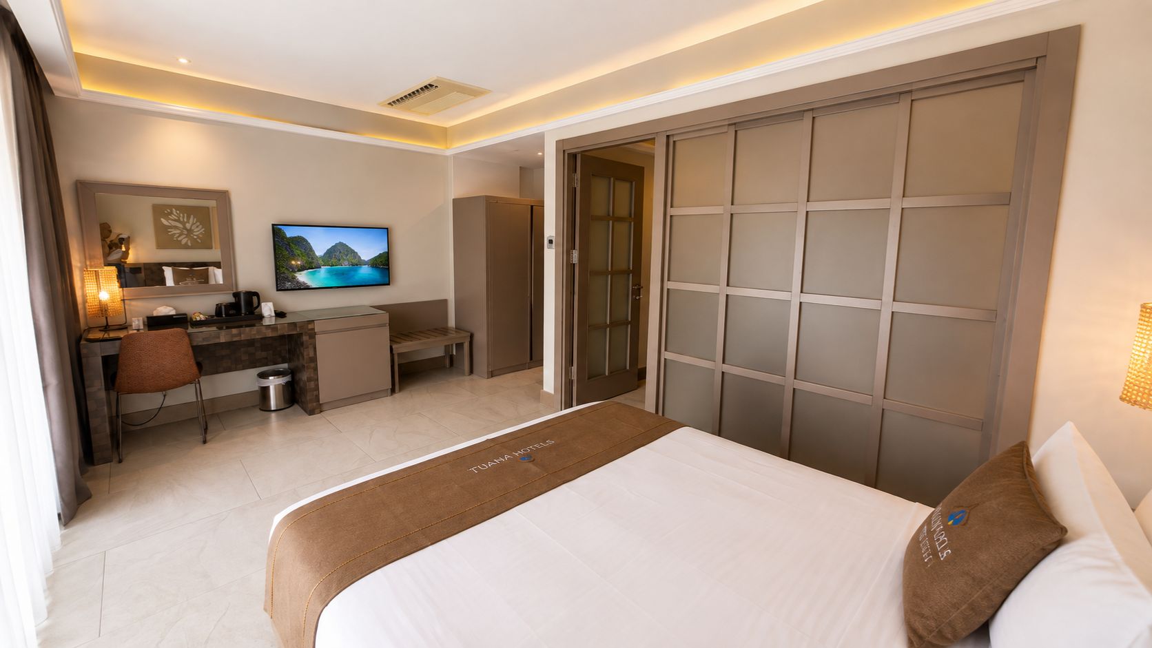 Habitació d'hotel amb llit, escriptori, televisió i porta corredissa.