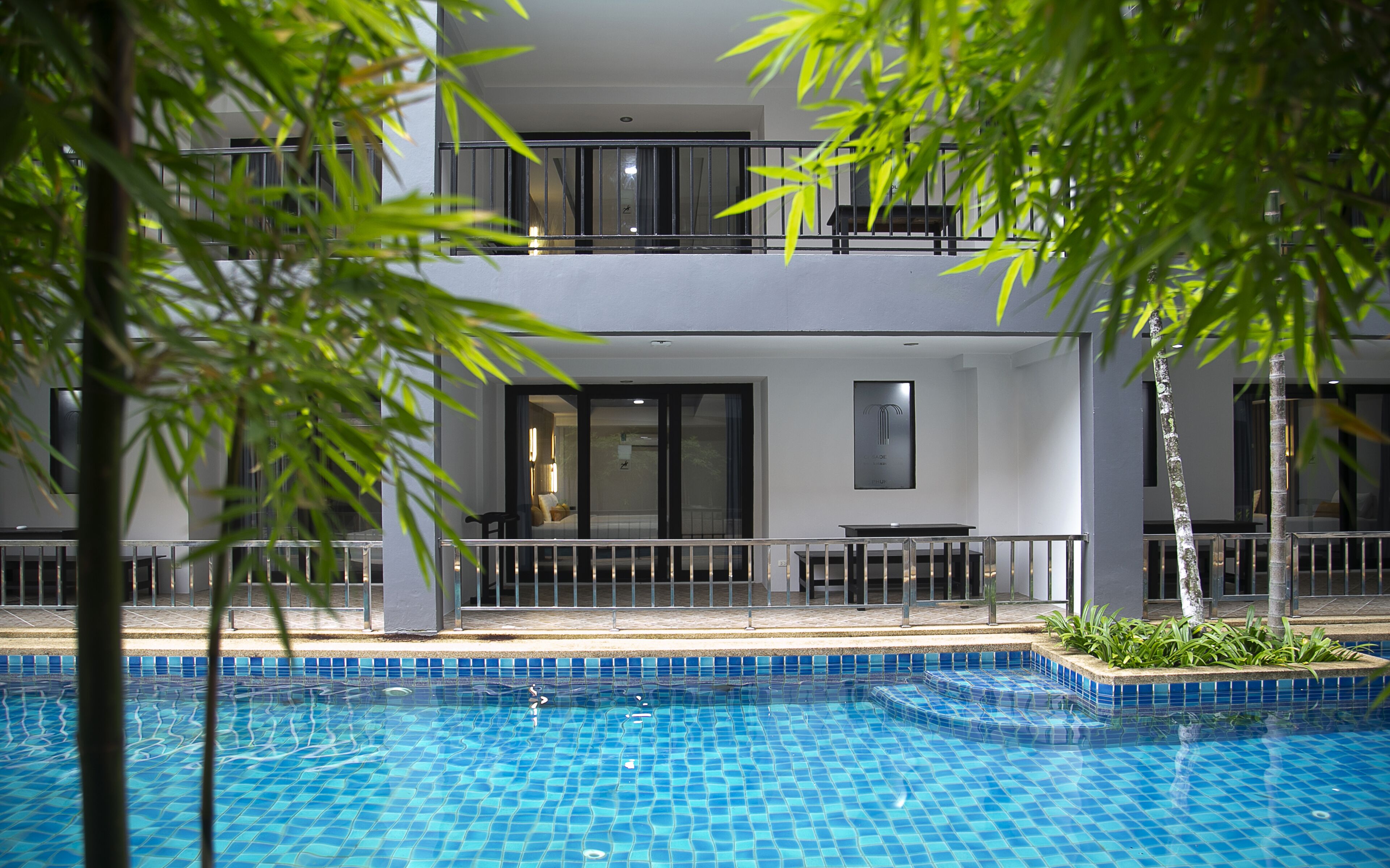 A modern hotel with a pool, featuring a two-story balcony with a seating area and a view of the pool.