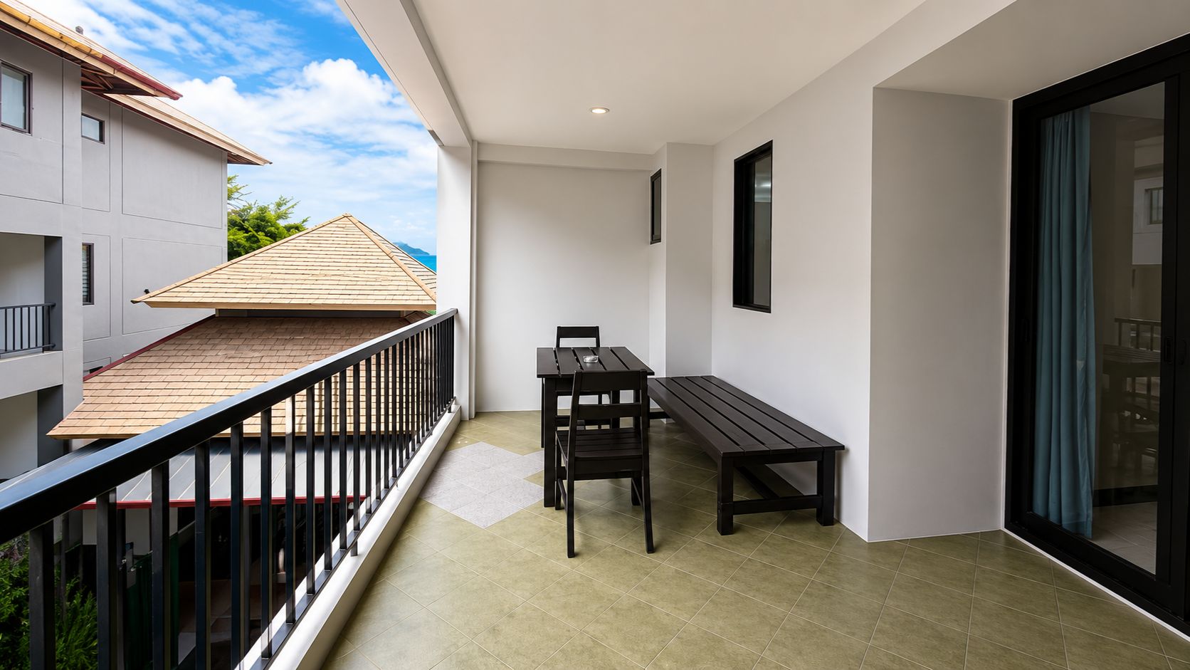 A balcony with a table and chairs, a wooden roof, and a view of a building with a tiled roof.