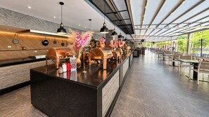 Un espace bar moderne doté d’un long comptoir, d’un éclairage suspendu et d’éléments décoratifs tels que des fleurs et des pots en cuivre.