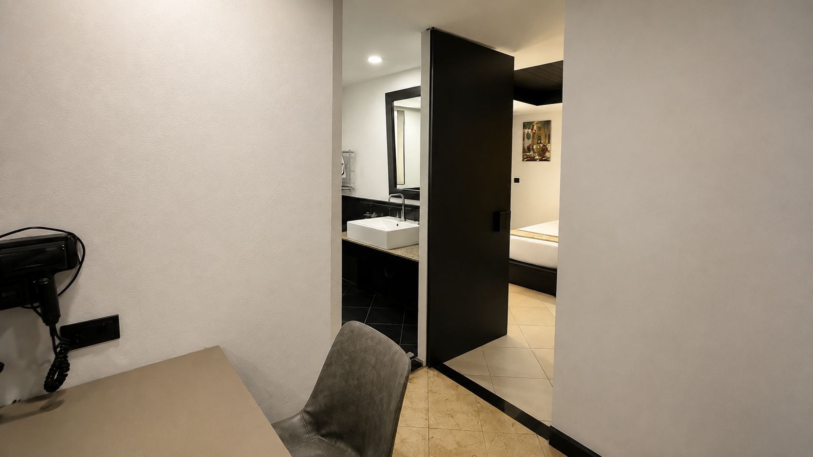 A modern bathroom with a white sink, a mirror, and a black door leading to a bedroom.