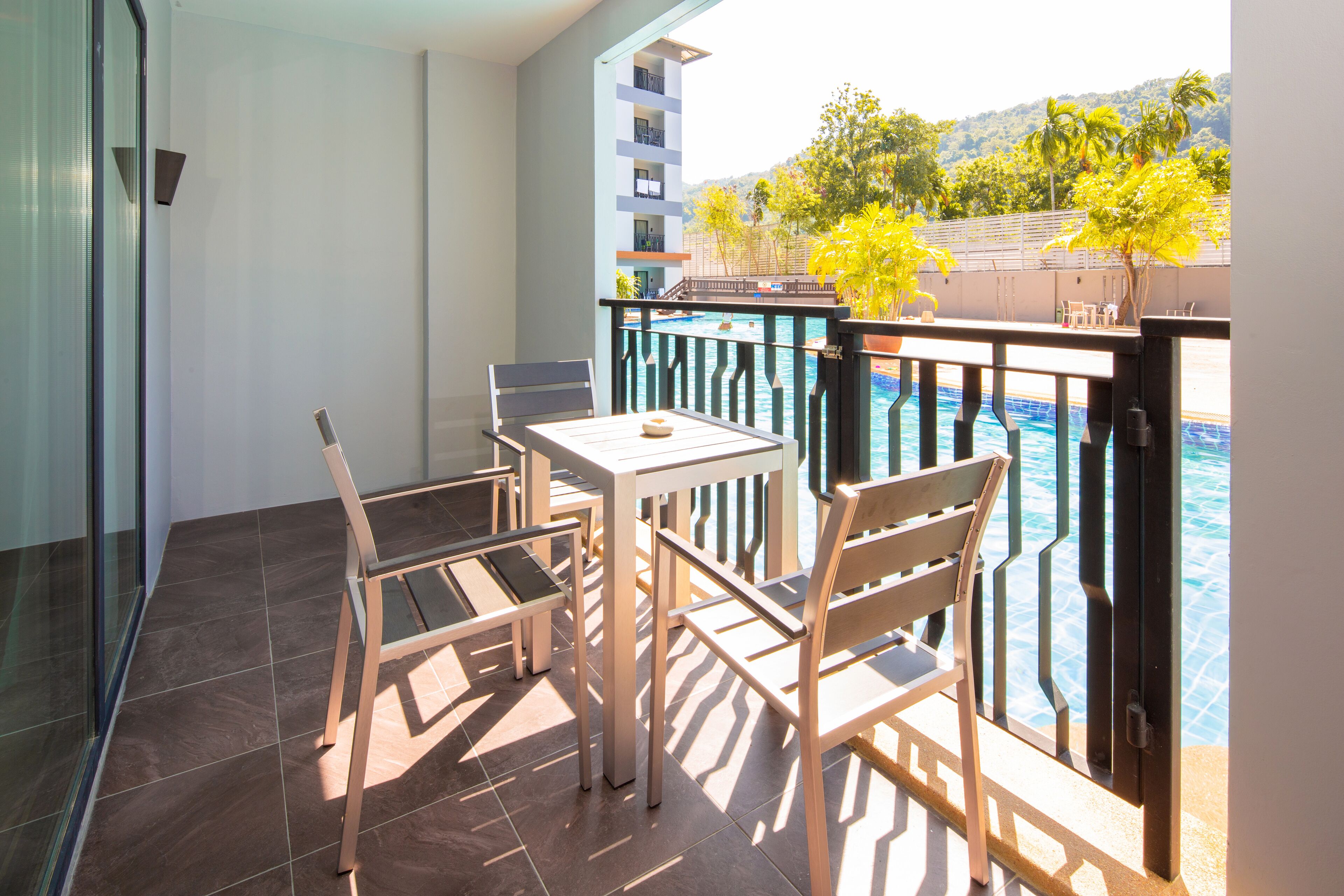 A balcony with a table and chairs, overlooking a swimming pool and a building with multiple floors.