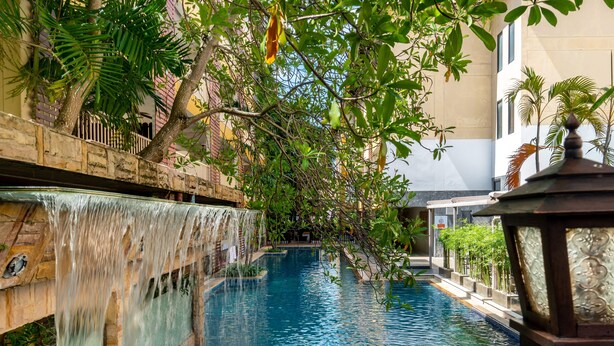 A pool with a waterfall feature, surrounded by lush greenery and a stone wall. - Tuana Hotels Casa Del Sol (Karon)