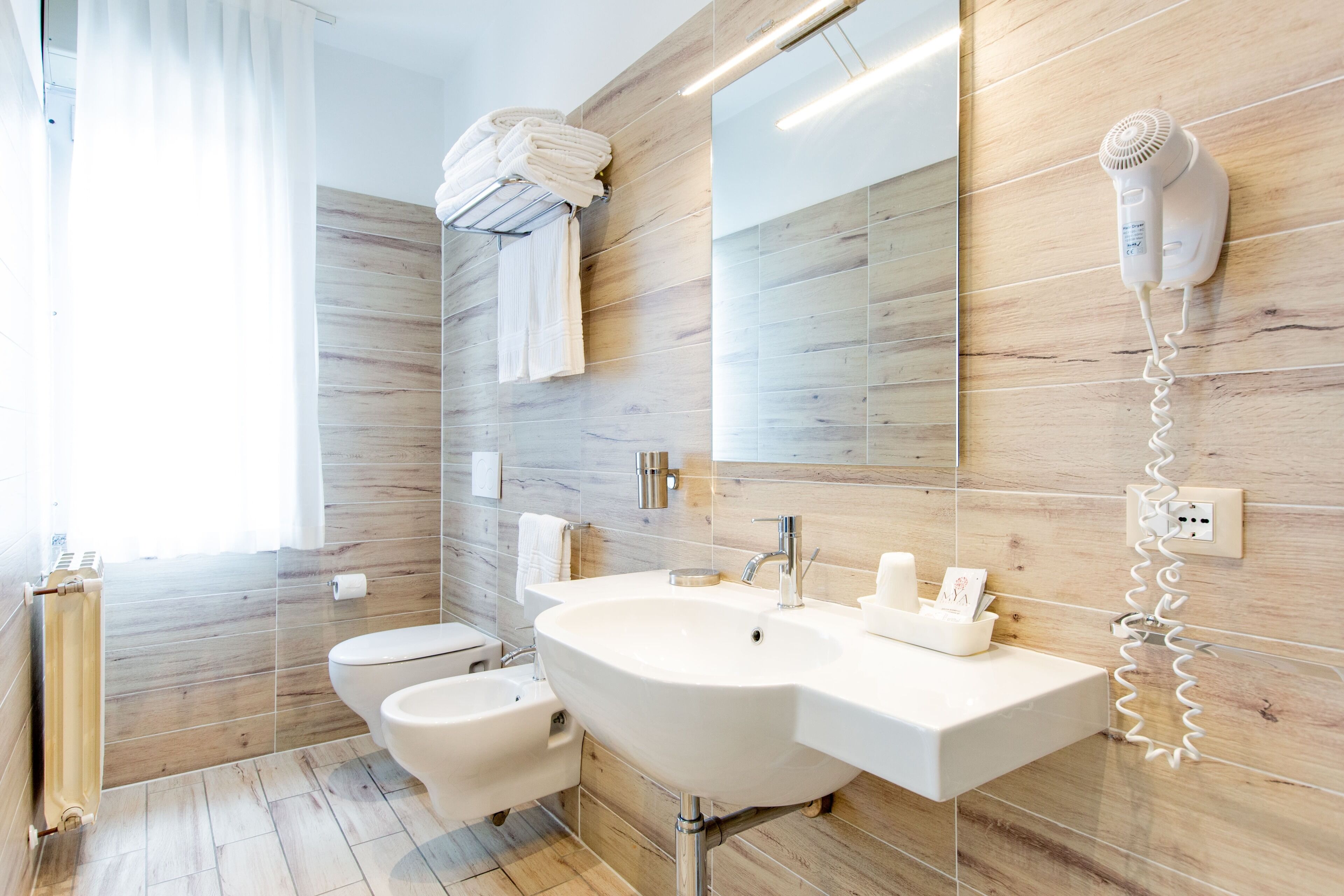 Un baño moderno con un lavamanos grande, un inodoro, un bidé, un perchero para toallas y un secador de pelo montado en la pared.