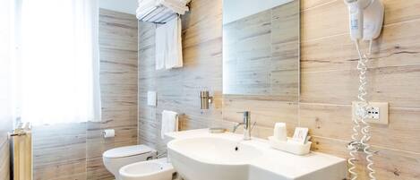 Un baño moderno con un lavamanos grande, un inodoro, un bidé, un perchero para toallas y un secador de pelo montado en la pared.