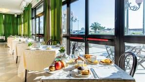 Un comedor con mesas dispuestas para el desayuno, con diversos alimentos y vistas al exterior.