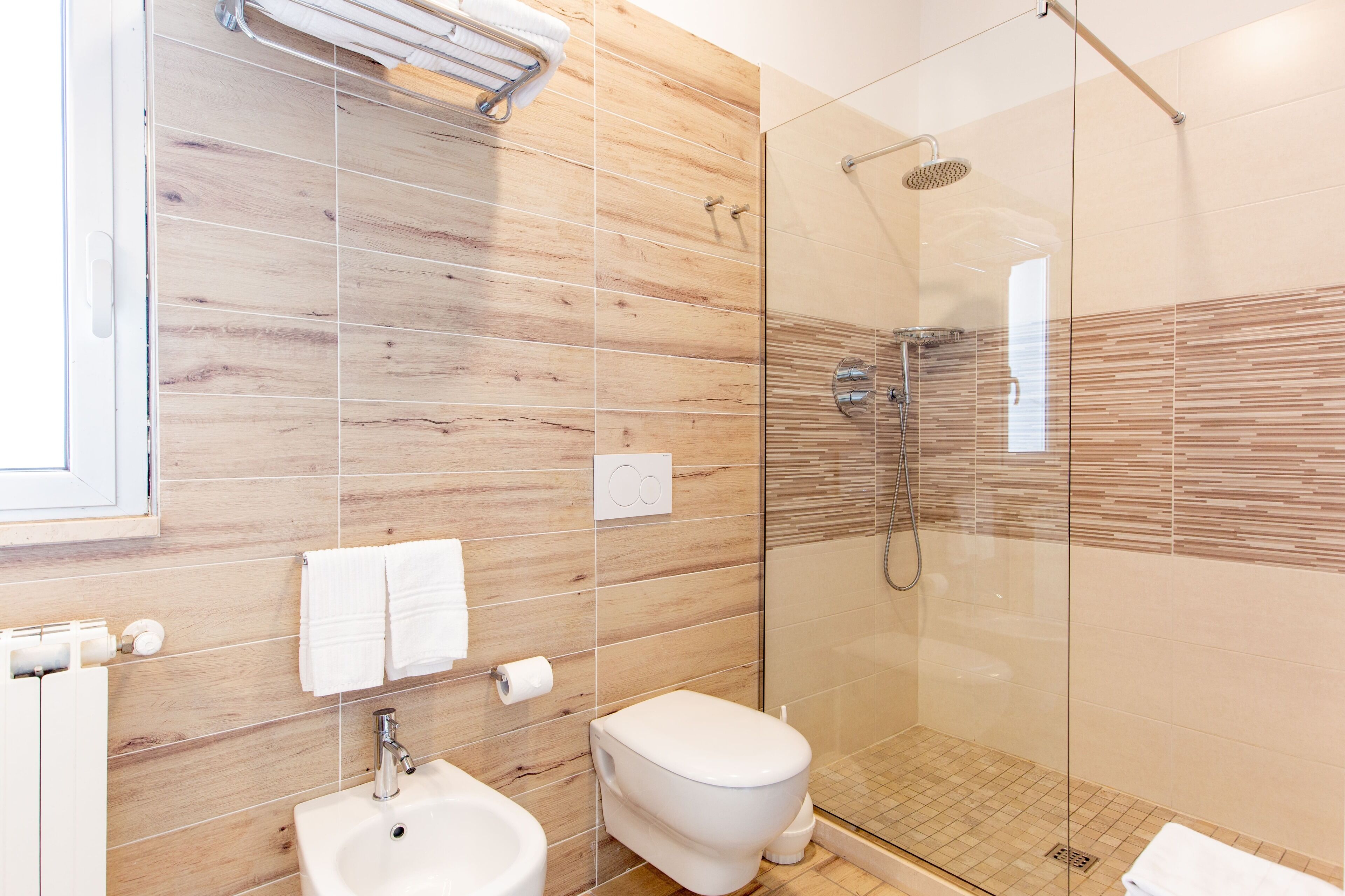 Un baño moderno con pared de madera, cabina de ducha de vidrio, lavamanos blanco y un inodoro.