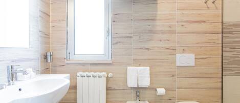 A modern bathroom with a white sink, bidet, and toilet, wooden wall tiles, and a window.
