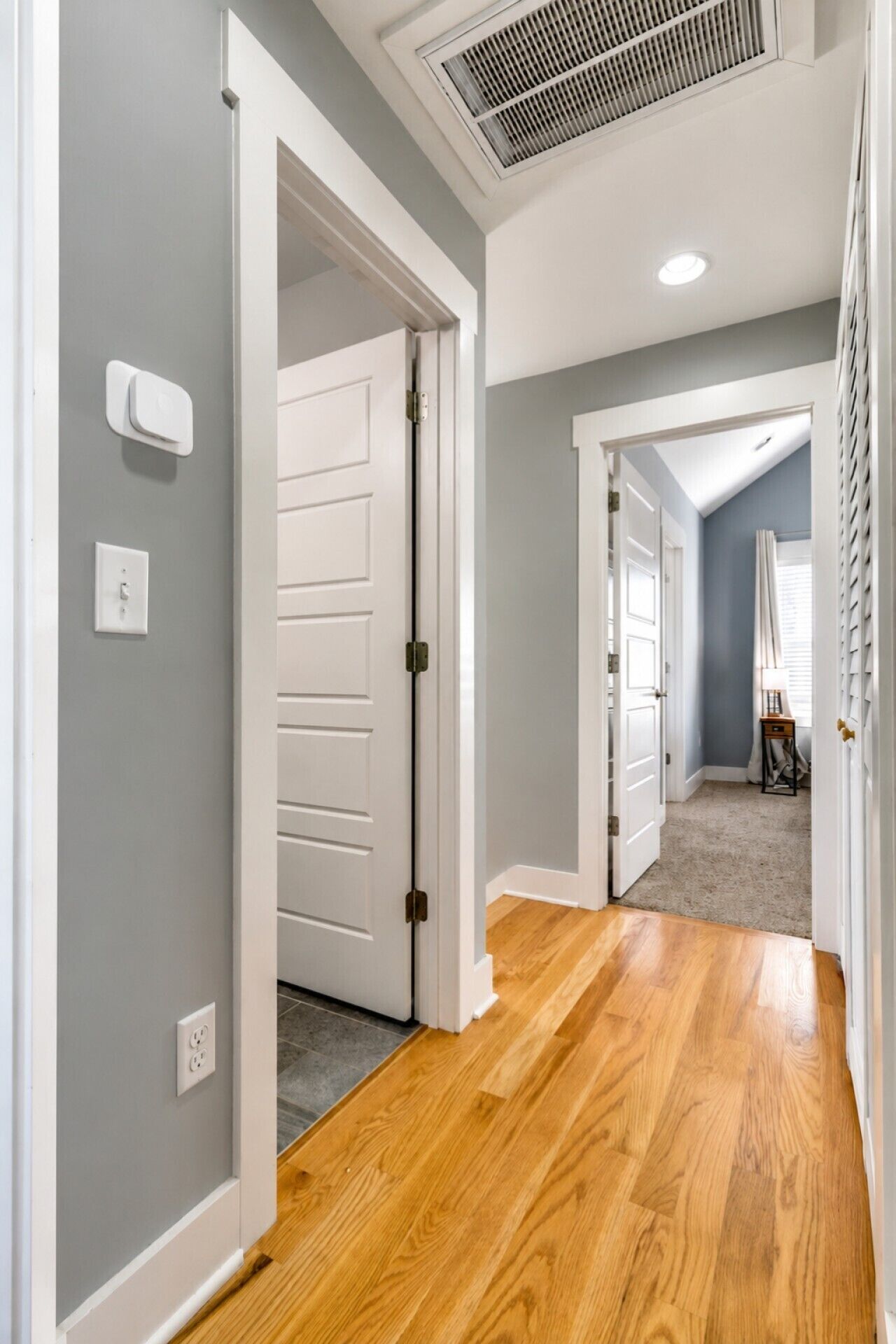 A hallway with wooden flooring, white doors, and a ceiling vent.
