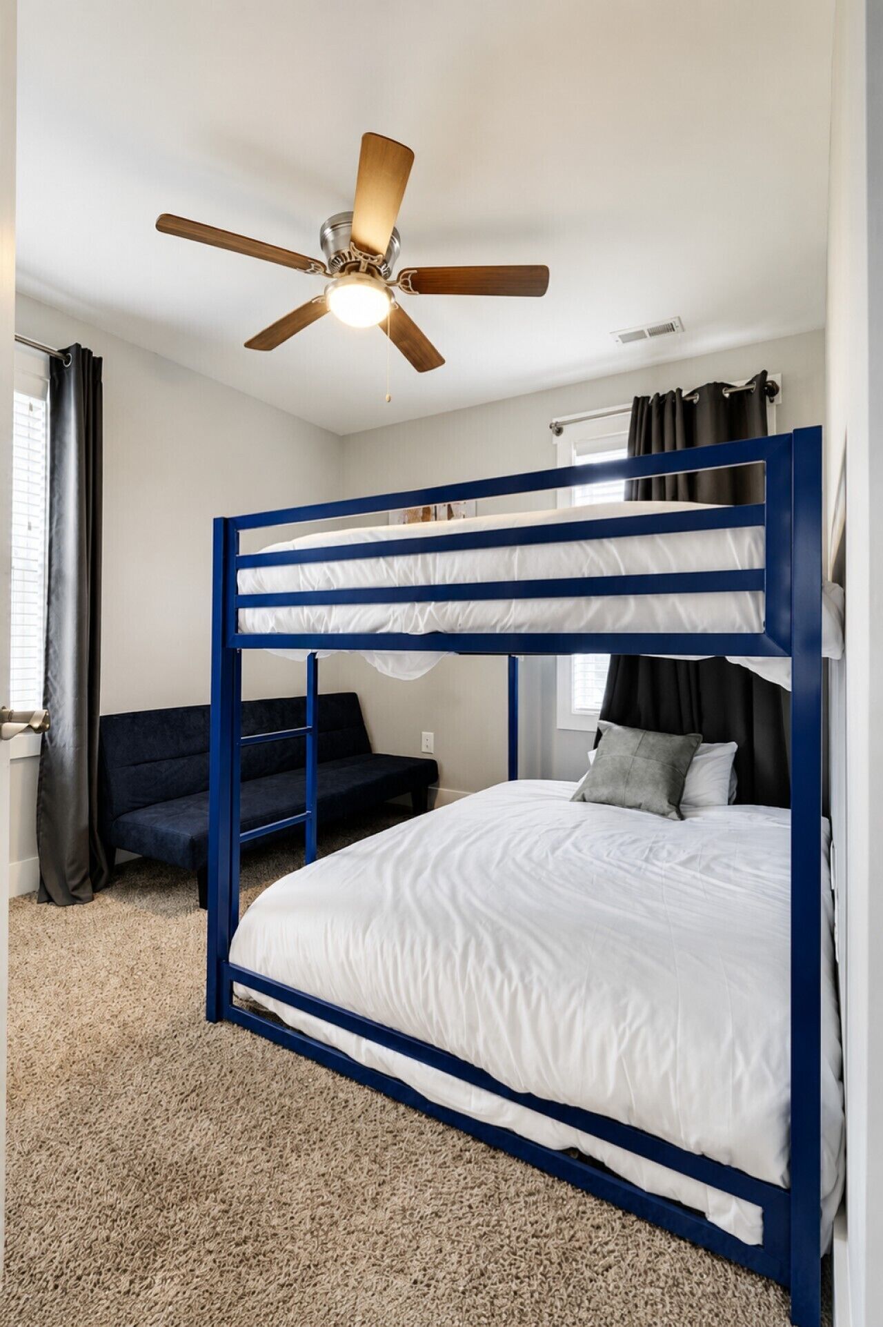 A bunk bed with a ceiling fan, a sofa, and a window with curtains.
