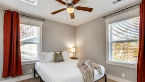 A bedroom with a bed, a ceiling fan, a nightstand, and a window with blinds.