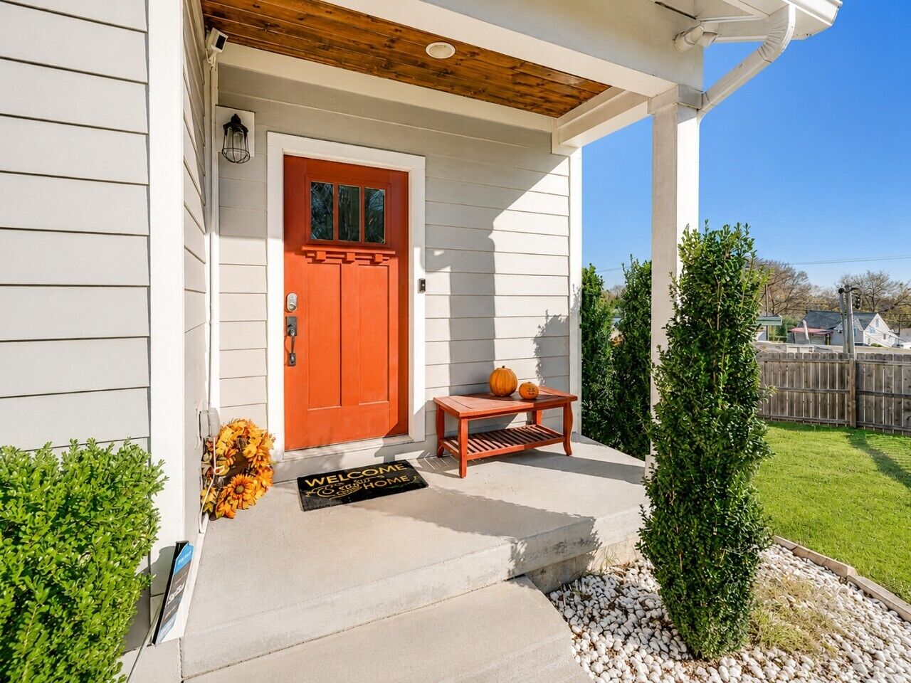 A house with a red door, a welcome mat, a small table with pumpkins, and a well-maintained lawn.