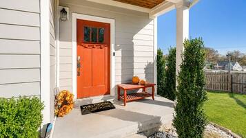 A house with a red door, a welcome mat, a small table with pumpkins, and a well-maintained lawn.