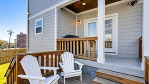 A house with a porch, two Adirondack chairs, a barbecue grill, and a wooden deck.