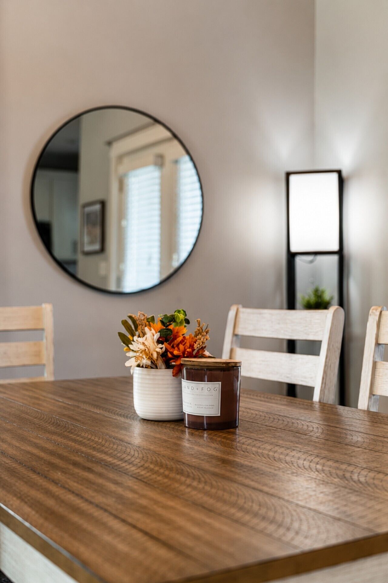 A dining table with a candle, a flower arrangement, and a mirror on the wall.