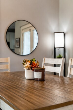Ein Esstisch mit Kerze, Blumenarrangement und Spiegel an der Wand.