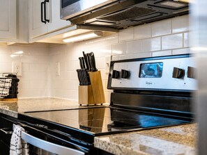 A kitchen with a black stove, white tiled backsplash, and a stainless steel range hood.