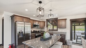 Uma cozinha moderna com eletrodomésticos de aço inoxidável, bancadas de granito e iluminação pendente.