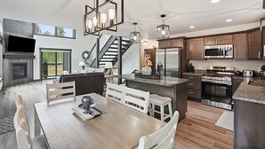 Uma cozinha moderna com ilha central, eletrodomésticos de aço inoxidável e área de jantar com mesa e cadeiras de madeira.