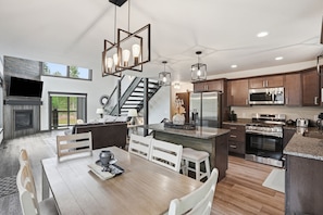 A modern kitchen with a central island, stainless steel appliances, and a dining area with a wooden table and chairs. - Pet friendly Embers Ultimate duplex, hot tub, wifi, paved roads, pool access (Lead)