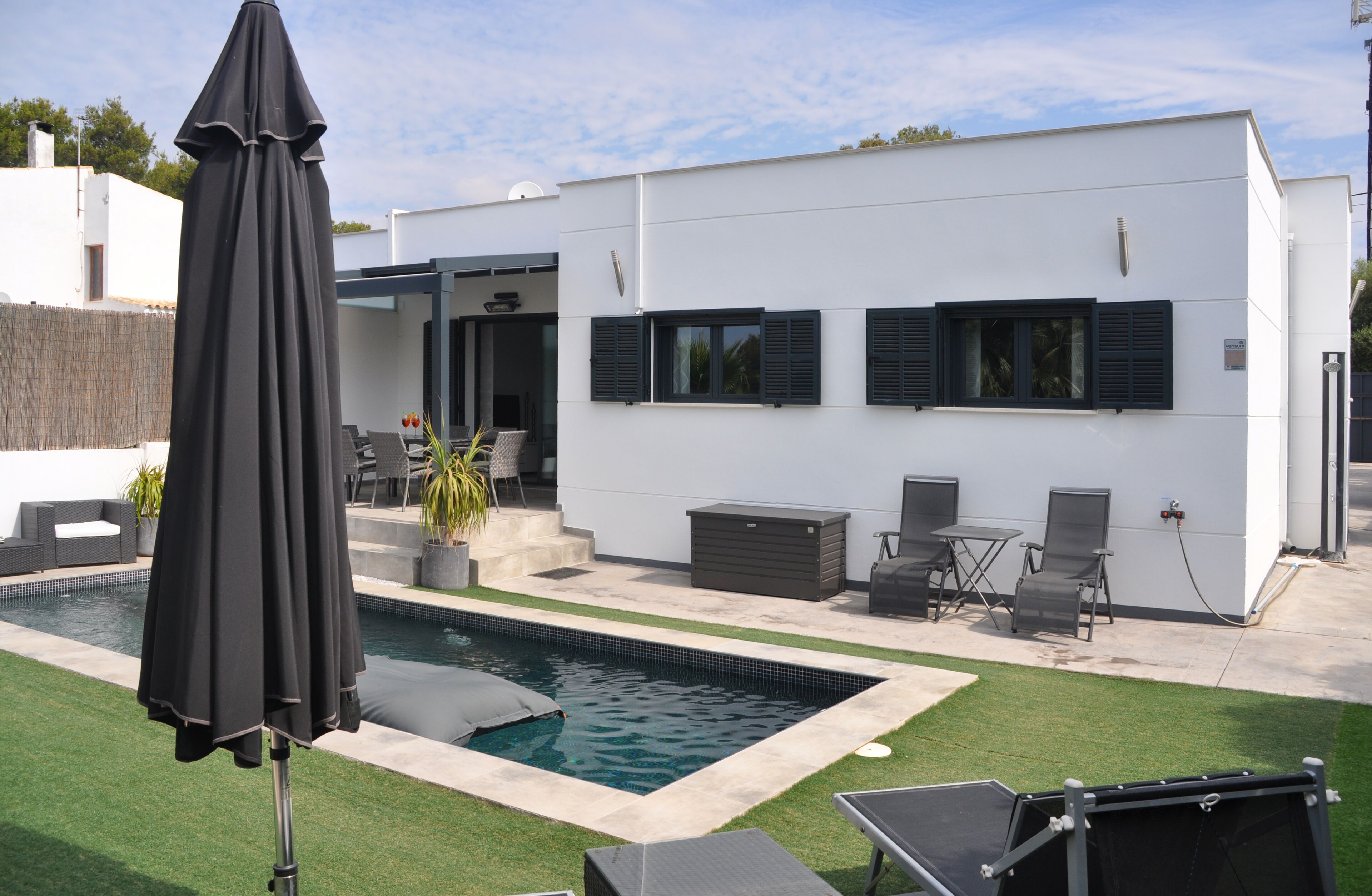 A modern outdoor pool area with a white building, black shutters, and outdoor furniture.