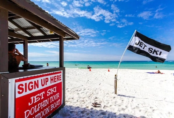 A beachside sign-up area for a Jet Ski and Dolphin Tour, with a clear view of the ocean and beach in the background.
