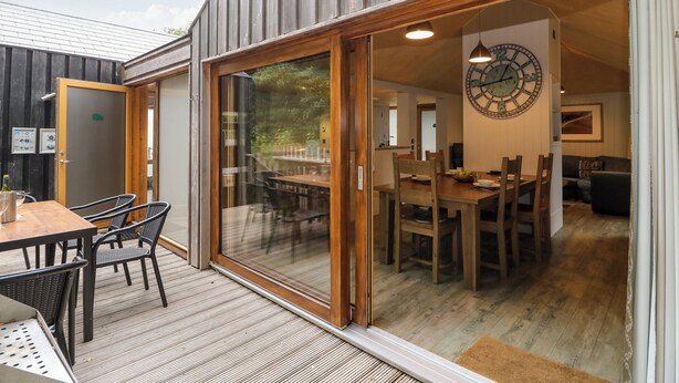 A wooden exterior with a sliding glass door leading to an interior dining area with a large wall clock. - Lodge 4 (Wareham)
