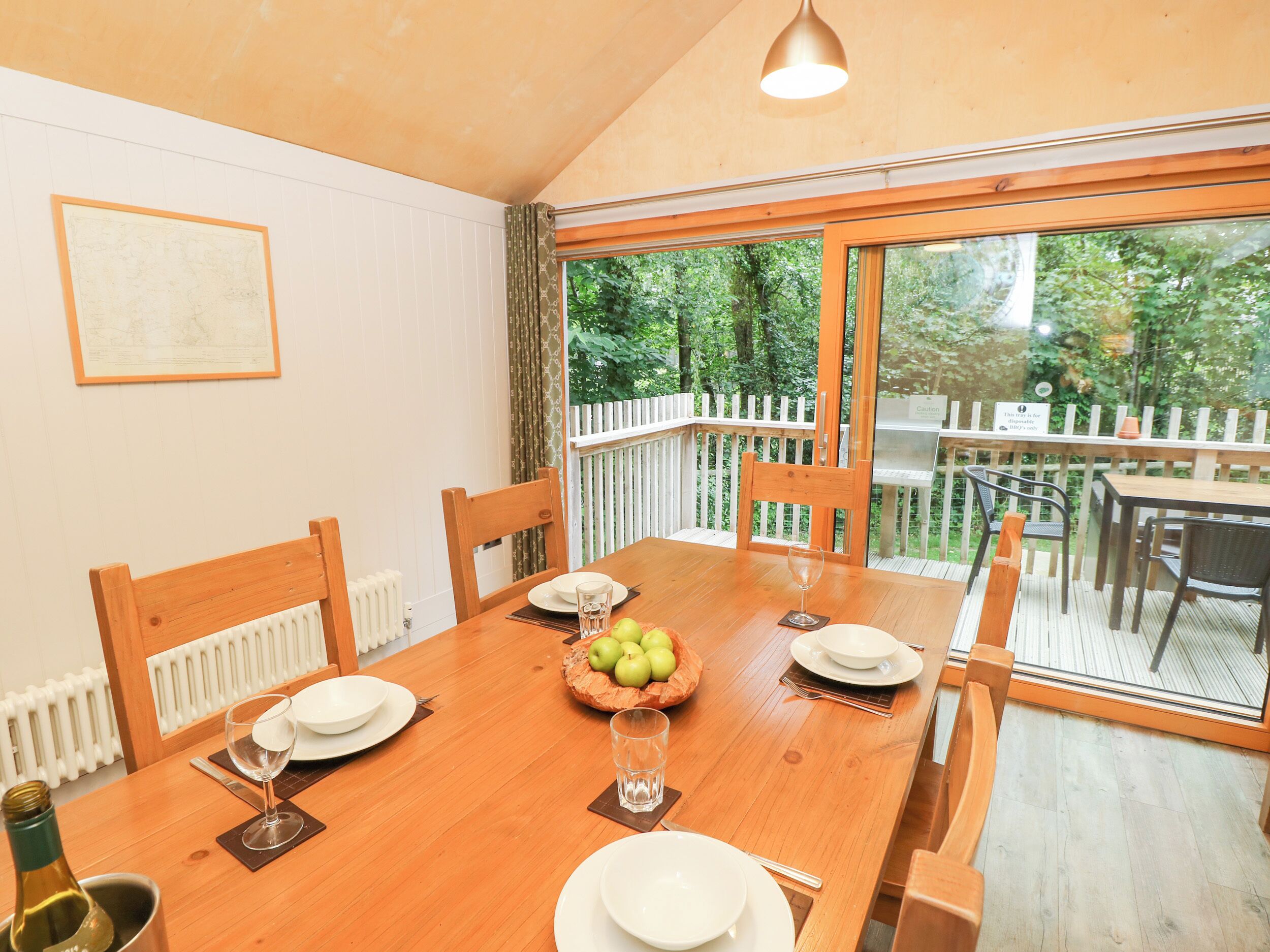 Un coin repas avec une table en bois dressée pour quatre personnes, entourée de chaises, et donnant sur un jardin grâce à de grandes portes vitrées.