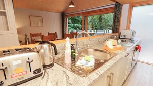 A kitchen with granite countertops, a toaster, a kettle, a sink, and a window with a view of greenery. - Lodge 4 (Wareham)