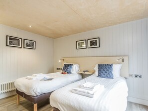 Une chambre d’hôtel avec deux lits, du linge de lit blanc, une tête de lit en bois, une table de chevet et des tableaux encadrés au mur.