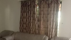 A living room with a beige sofa, a glass coffee table, and patterned curtains. - Impeccable 4-bed Villa in Mirpur Azad Khasmir (Mirpur)