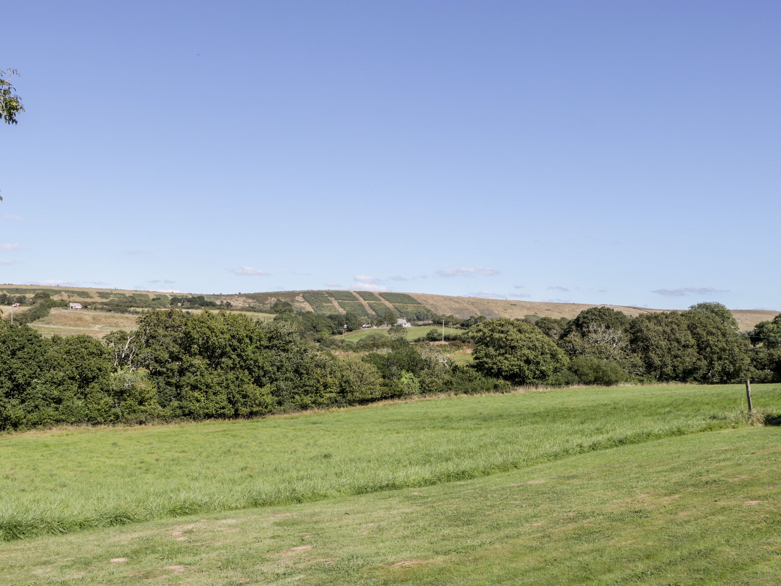 A rural landscape with rolling hills, a clear sky, and a grassy field.