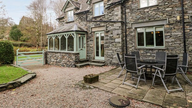 A stone house with a conservatory, a gravel driveway, and a patio with outdoor seating. - Scandale Bridge Cottage (Ambleside)