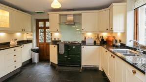 A kitchen with white cabinets, a black countertop, and a green stove. There is a window with a view of trees and a door leading to another room. - Scandale Bridge Cottage (Ambleside)