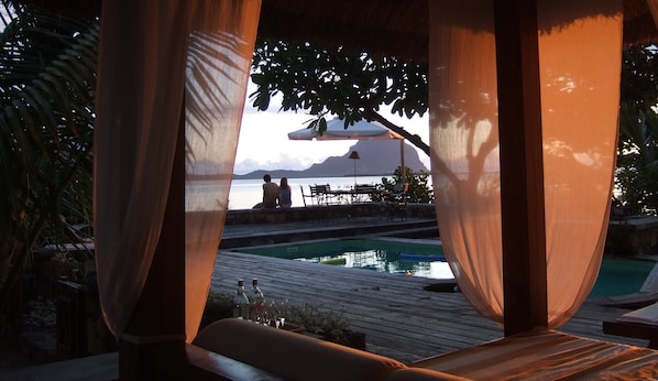 A wooden deck with a pool, overlooking a body of water with mountains in the background.