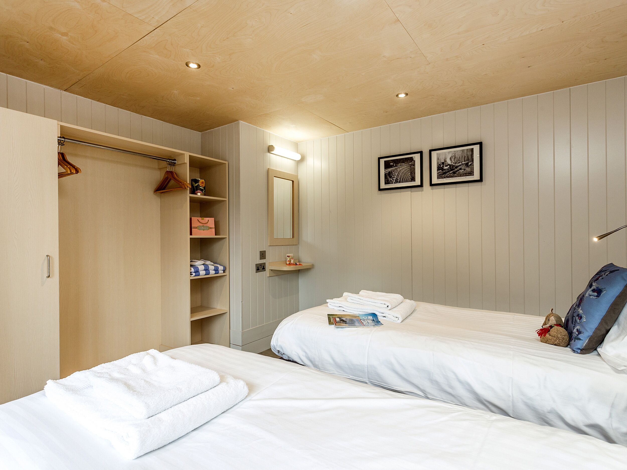 Une chambre d’hôtel avec deux lits, une armoire, un miroir et deux tableaux encadrés au mur.