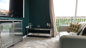 A living room with a green accent wall, a white sofa with patterned cushions, a marble-patterned rug, a metal crib, and a television on a stand. - Beautiful 1-bed Apartment in Redhill (Redhill)