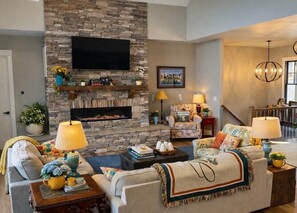 A cozy living room with a stone fireplace, comfortable sofas, and a flat-screen TV mounted above it. - Waterfront 5BD/5BA Private Dock & 9P-Hottub (Six Mile)