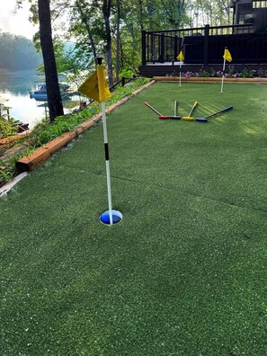 A miniature golf course with a green artificial turf, a blue ball in a hole, and yellow flags marking the course.