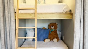 Kerrossänky, jossa on puinen tikapuut, pehmolelu ja sininen tyyny.