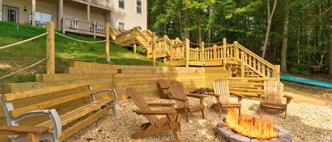 A wooden deck with outdoor seating, a fire pit, and a staircase leading to a building.