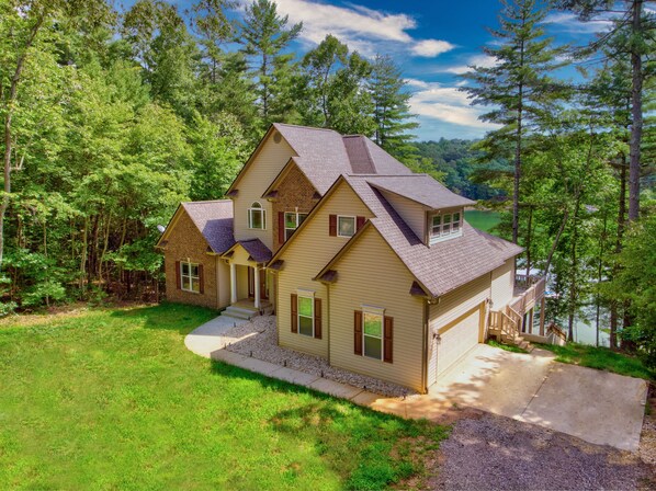 A two-story house with a large garage, surrounded by a forested area.