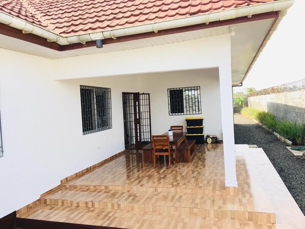 Un patio cubierto con suelo de madera, una mesa con sillas y un banco.