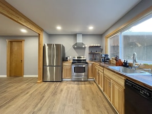 A modern kitchen with stainless steel appliances, wooden cabinets, and a large window.