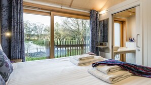 A bedroom with a large bed, a bathroom with a mirror, and a view of a garden through the window. - Lodge 10 (Wareham)