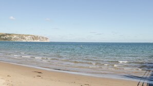 A beach with calm waters, a sandy shore, and a cliff in the background. - Lodge 10 (Wareham)