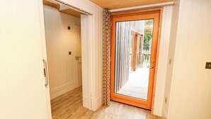 Un pasillo con suelo de madera, paredes blancas y un divisor de vidrio corredizo que da a un área exterior con terraza de madera.