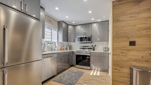 A modern kitchen with stainless steel appliances, grey cabinetry, and a wooden accent wall. - Ski on/off home in Camelback (Tannersville)