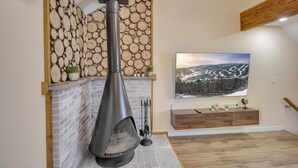 A modern living room with a stone wall, a fireplace, a TV, and a wooden bench. - Ski on/off home in Camelback (Tannersville)